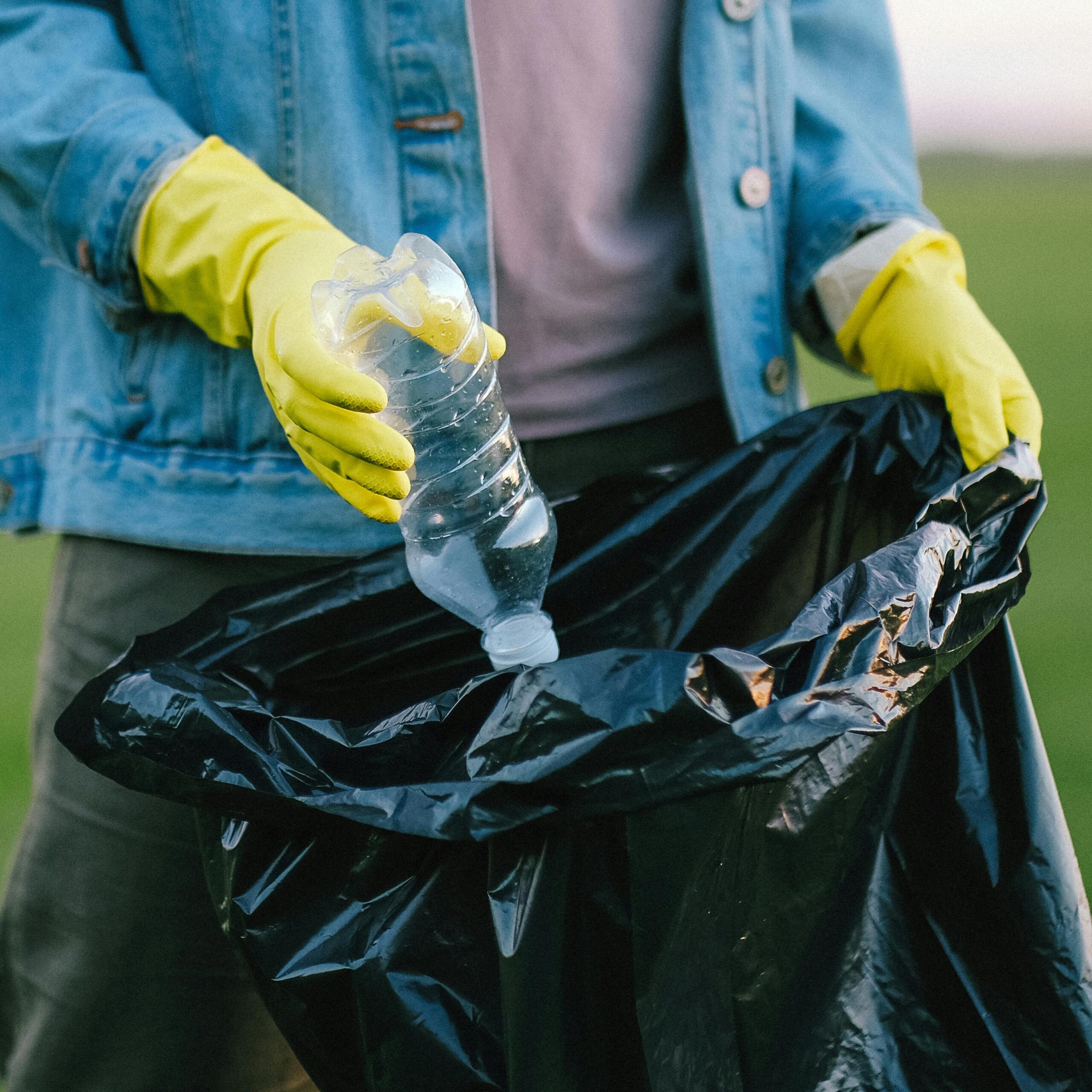 A person wearing rubber gloves puts a plastic water bottle in a trash bag