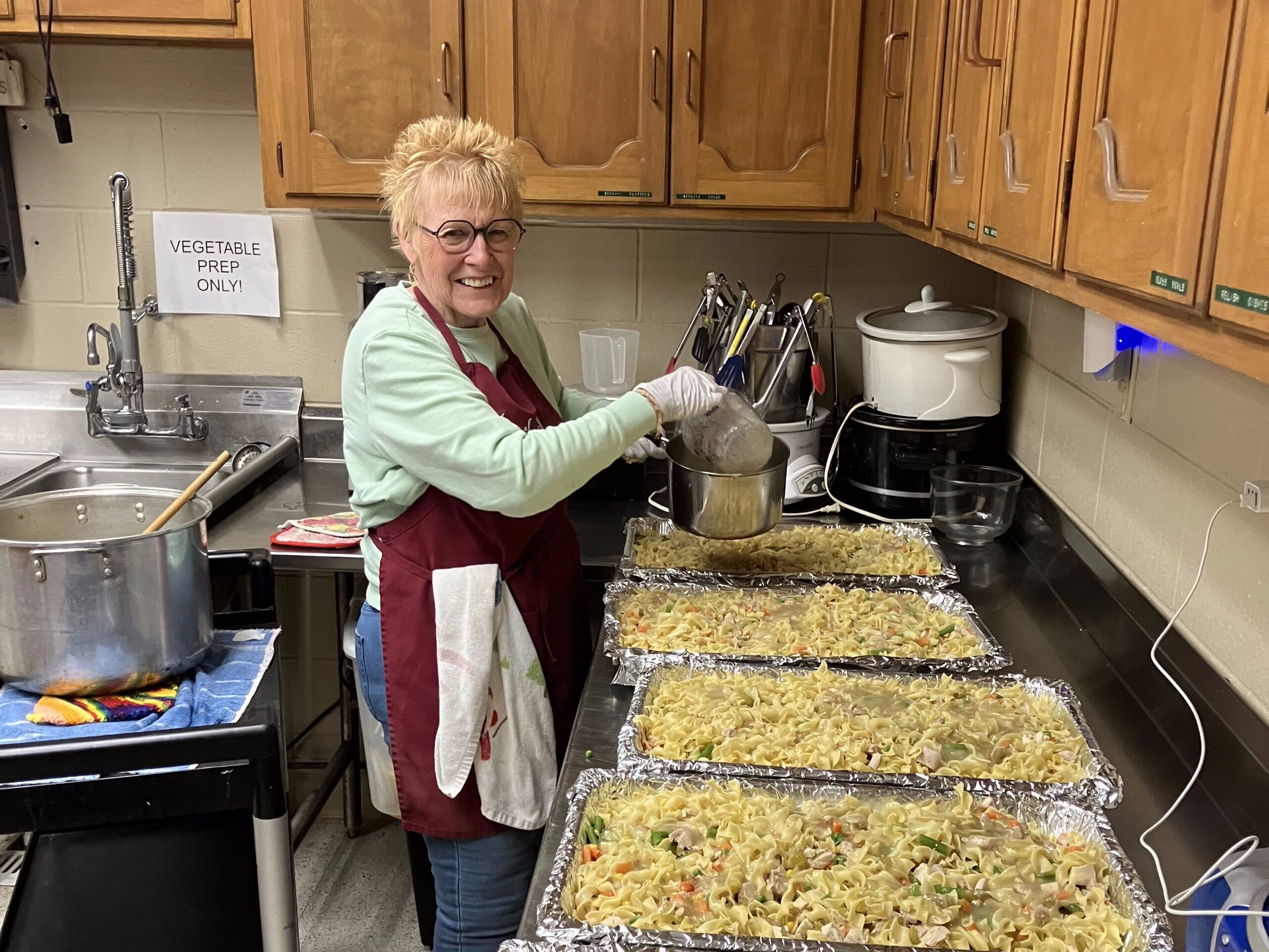 A volunteer prepares multiple trays of food for a community meal.