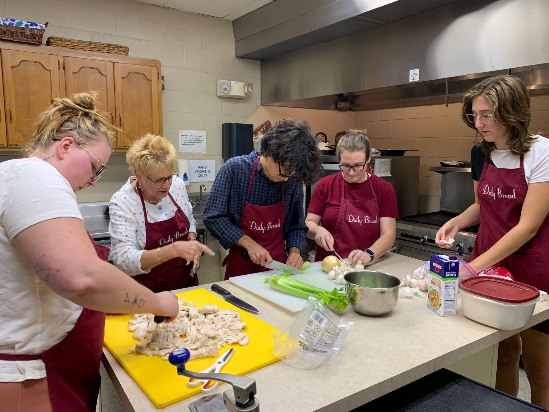 A group of young adults prepare a meal in a kitchen guided by an instructor